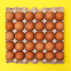 Organic eggs in cardboard box on vibrant yellow background. Flat lay Easter food