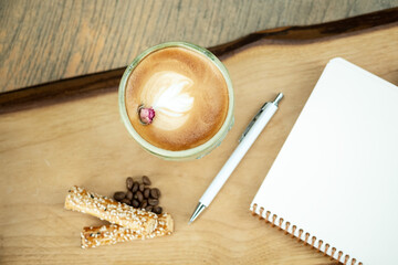 Empty notebook, white pen and cappuccino coffee on wooden table, top view.