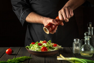 Chef adds peppers to a fresh vegetable salad in a restaurant kitchen. Close-up of cook hands holding a mill. Cooking healthy and tasty food