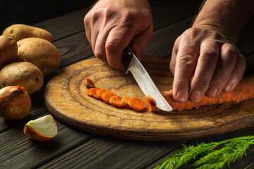 Chef is cutting carrots for vegetable soup in the restaurant kitchen. Close-up of the hands of the cook during work. Carrot diet