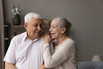 Happy laughing older married couple talking, laughing, standing in home interior together, hugging with love, enjoying close relationships, trust, support, care, feeling joy, tenderness