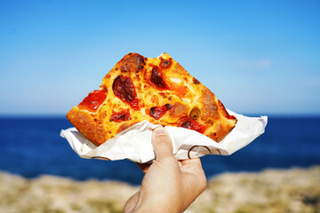 Focaccia barese slice with Mediterranean sea on background. Focaccia pugliese against blue sea and...
