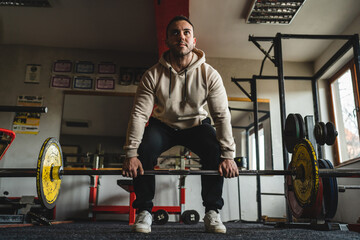 Fototapeta na wymiar One man young adult caucasian male bodybuilder training back doing deadlift with barbel and weights while standing in the gym wearing hoodie real people copy space front view full length