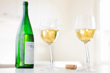 Two glasses  with white wine and green wine bottle in a bright room