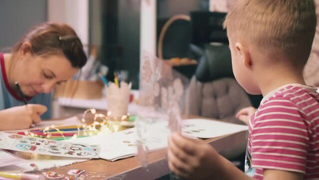 After the New Year holidays, mother and son have a good time, together drawing and glue vinyl stickers in the form of santa claus.