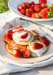 Cheesecakes with strawberries and sour cream. Breakfast in nature. Traditional Russian and Ukrainian dish.