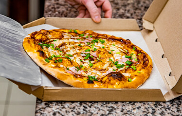 Cooked hot pizza with chicken and barbeque sauce on a shovel is put into a packing box, food delivery