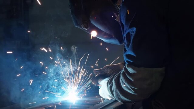Close-up of metal welding, blue glow, red sparks flies, welding arc, metal melts, metal construction