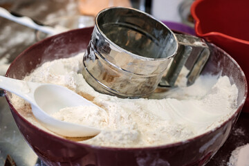 metal flour sifter in brown bowl with flour and white spoon