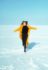 Young running woman in yellow coat walking on snowy ice. 