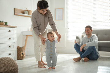Mother supporting her baby daughter while she learning to walk at home