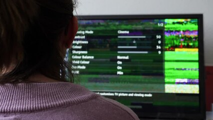Rear view of woman trying to repair the broken tv bad signal from aerial inside the menu of the tv-set - searching for better frequencies on the DBVT frequency range