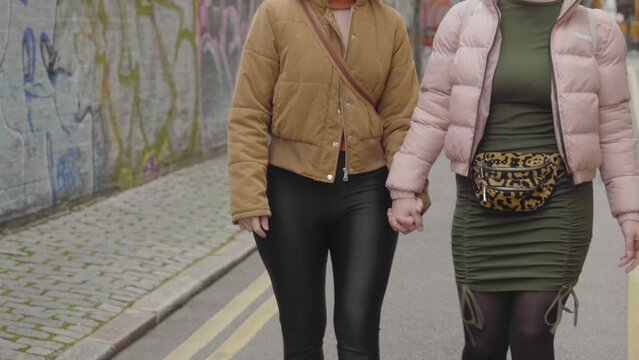 Same gender lesbian couple holding hands while walking down the street, unrecognizable middle shot