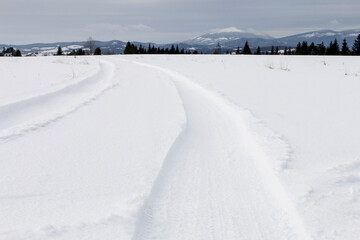 Fototapeta na wymiar Vehicle wheel traces on snow, mountains in the background.