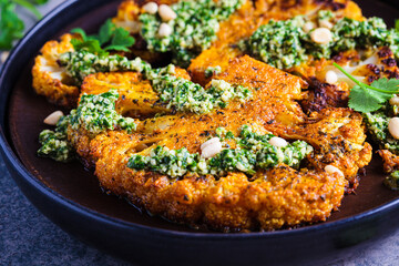 Spicy grilled cauliflower steaks with homemade green pesto on wooden plate.