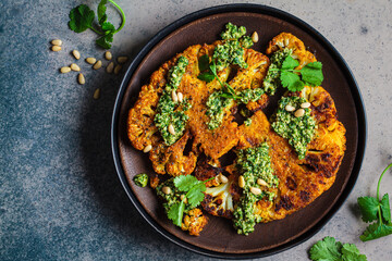 Spicy grilled cauliflower steaks with homemade green pesto on wooden plate.