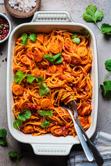 Baked spaghetti pasta with sausages in tomato sauce in oven dish.