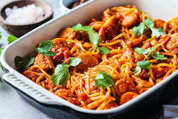 Baked spaghetti pasta with sausages in tomato sauce in oven dish.