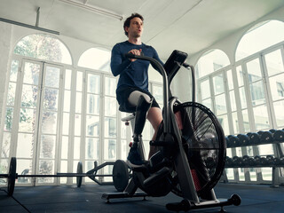 Obraz na płótnie Canvas Disabled athlete man riding an airbike in a modern gym 