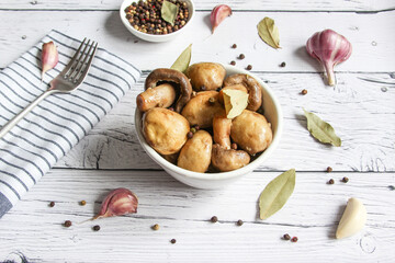 Champignons marinated, pickled mushrooms with spice in bowl on the wooden background. Marinated mushrooms with garlic, black pepper and bay leaf. 