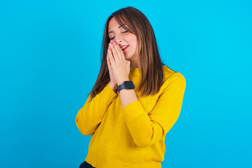Overjoyed Young arab woman wearing knitted sweater over blue backgtound  laughs joyfully and keeps...