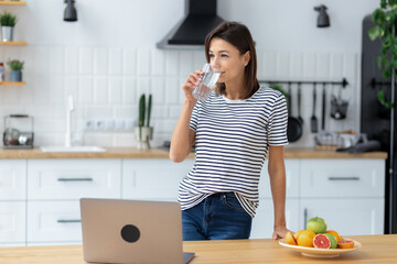 Portrait of Happy caucasian woman standing with glass of clean water at home kitchen. Healthy...