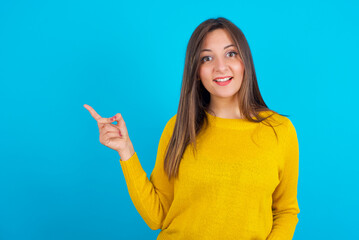 Young arab woman wearing knitted sweater over blue backgtound points aside on copy blank space. People promotion and advertising concept