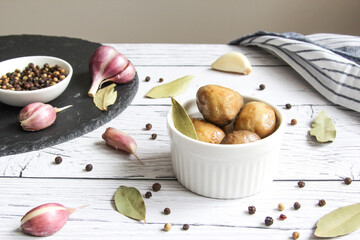 Pickled mushrooms with spice in bowl on the wooden background. Champignons marinated. Marinated mushrooms with garlic, black pepper and bay leaf. 