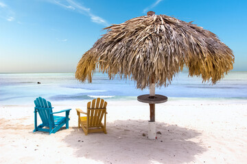 Straw parasol and colorful chairs on a tropical sandy beach
