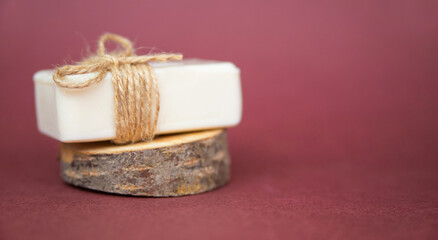 A piece of white soap lies on a cut of a tree on a burgundy background. A natural organic product.