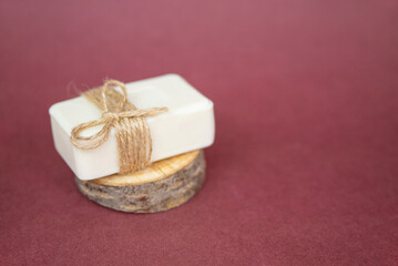 Fototapeta na wymiar A piece of white soap lies on a cut of a tree on a burgundy background. A natural organic product.