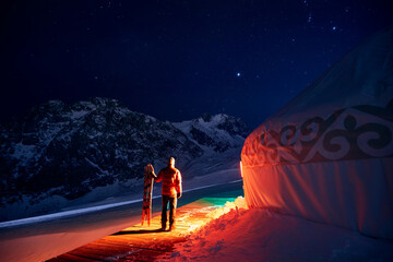 Man with snowboard near Yurt nomadic house at night at Mountains
