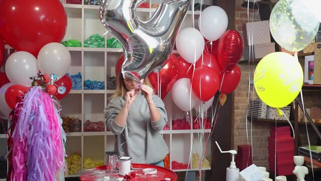 a woman inflates a balloon in the shape of a large silver numeral for a birthday