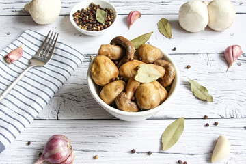 Pickled mushrooms with spice in bowl on the wooden background. Champignons marinated. Marinated mushrooms with garlic, black pepper and bay leaf. 