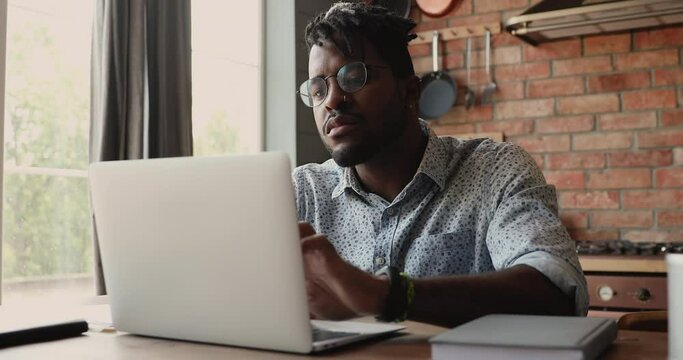 Serious young Afro American self employed businessman work freelance at home office browse web use internet service on modern touchscreen laptop. Millennial male engaged in online job elearning on pc