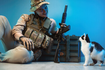 a male soldier in camouflage is sitting on the floor by a box of ammunition with weapons next to a...
