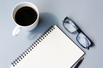 Notepad with cup of coffee and reading glasses on a desk. Directly above.