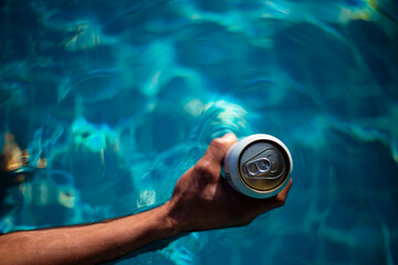 Selective focus white beer can in hand. Man is soaking in the pool with an open beer can relax and enjoy the holidays.