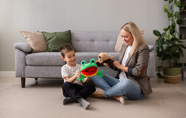 a little boy with his mother is sitting on the carpet near the sofa and playing puppet theater with a monkey and a frog