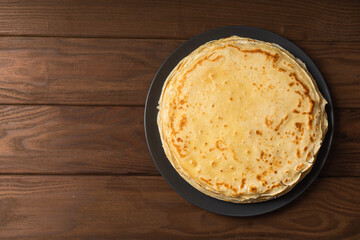 Pancake on the black plate on wooden table. Top view