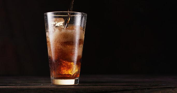 uring the liquid into the cola glass full of ice cubes. Isolated on dark background.