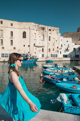 Fototapeta na wymiar Woman with a blue dress in the picturesque marina of Monopoli, a a little village in south Italy in summer