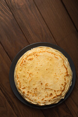 Pancake on the black plate on wooden table. Top view