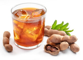 Glass of cool refreshing tamarind drink and some tamarind fruit on white background.