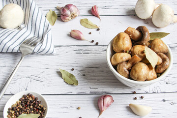 Pickled mushrooms with spice in bowl on the wooden background. Champignons marinated. Marinated mushrooms with garlic, black pepper and bay leaf. 