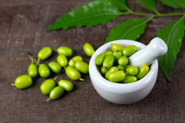 Fresh Neem fruit on white mortar with pestle and neem green leaf on rustic wooden background.