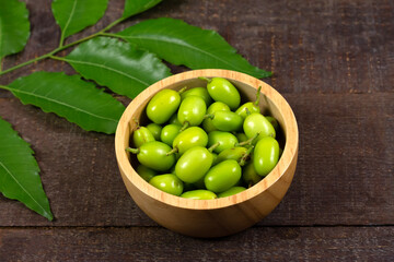 Fresh Neem fruit on wooden bowl and neem green leaf on rustic wooden background.