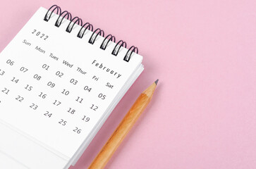February 2022 desk calendar with wooden pencil on pink background.