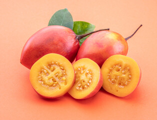 Naklejka na ściany i meble Ripe tamarillo fruits with slices and tamarillo leaves isolated on a orange background.