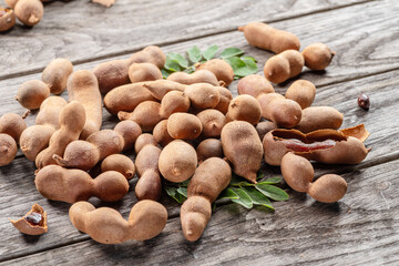 Ripe tamarind fruit, leaves and some tamarind seeds on wooden table.